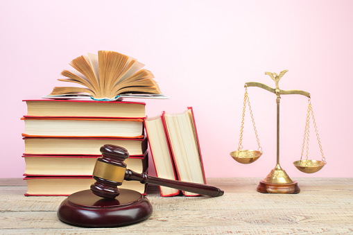 Law concept - Open law book, Judge's gavel, scales, Themis statue on table in a courtroom or law enforcement office. Wooden table, pink background.