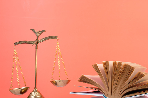 Law concept - Open law book, Judge's gavel, scales, Themis statue on table in a courtroom or law enforcement office. Wooden table, orange background
