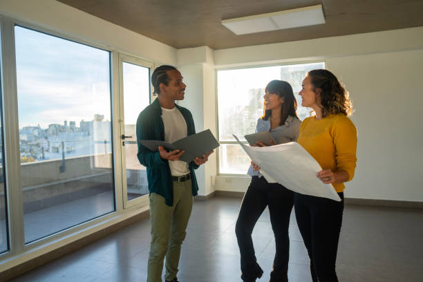 istock Female architect holding blueprint while explaining renovation plans with diverse couple 2150687014