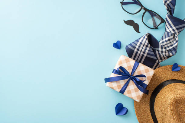 istock Stylish Father's Day gifts displayed on a blue background, including a hat, checkered gift box, tie, and sunglasses 2150688869
