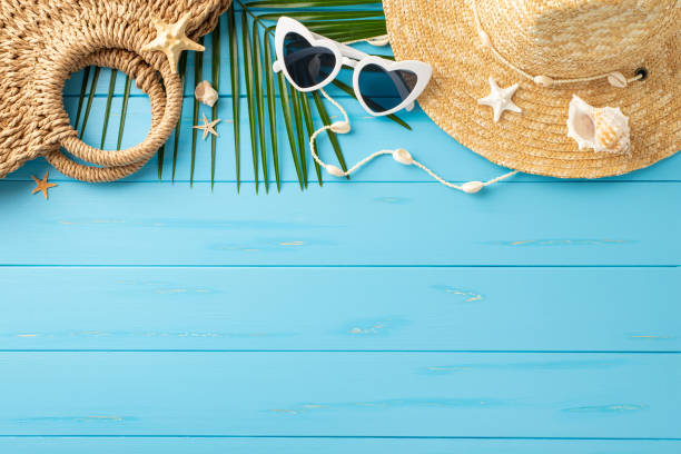 istock A cheerful summer vacation setup featuring a straw hat, sunglasses, a beach bag, seashells, and palm leaves arranged on a bright blue wooden surface 2150688878