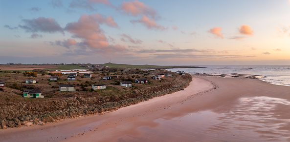 Aerial panorama landscape view of remote beach hut with a sea view on the Northumbrian sand dunes over looking Embleton Bay and Dunstanburgh Castle at sunset