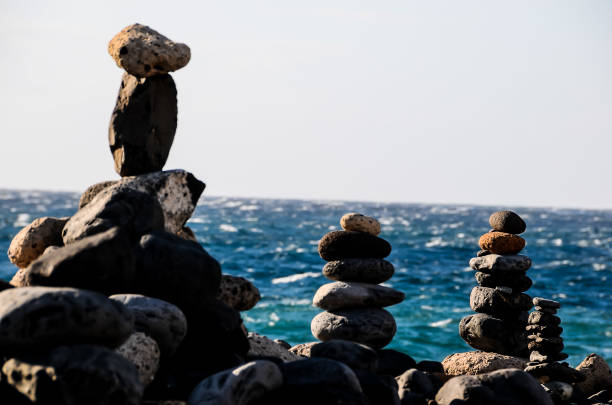 A stack of rocks is on the beach next to the ocean. The rocks are arranged in a pyramid shape, and the ocean is in the background. Concept of tranquility and peacefulness, as the rocks