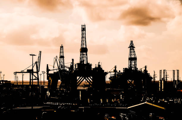 A city skyline with a large oil rig in the middle. The sky is cloudy and the sun is setting