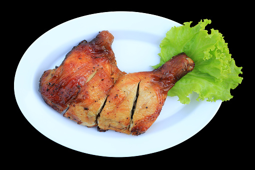 Roasted chicken leg on white plate isolated on black background. Top view.