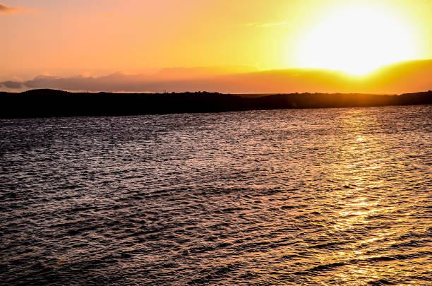 The sun is setting over the water, creating a beautiful and serene atmosphere. The water is calm and still, reflecting the warm colors of the sky. The scene is peaceful and relaxing