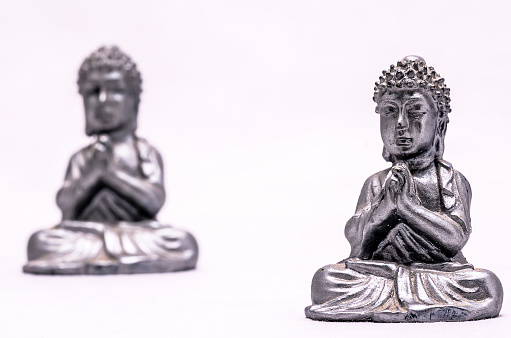 Two silver statues of Buddha sitting cross legged. One is on the left and the other on the right