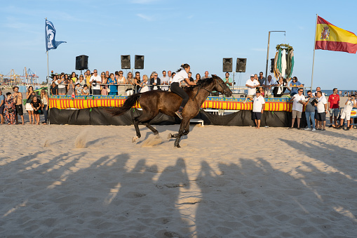 Pinedo (Valencia), Spain - September 17, 2022: A horsewoman crosses the finish line at high speed in front of the VIP box in a traditional bareback race on the beach of Pinedo, Valencia