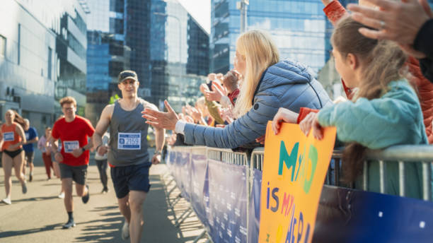 istock Marathon Audience Supporting and Cheering Their Loved Ones Participating in the Race: Athletic Male Marathon Runner Giving a High Five to Female Family Member in the Audience While Running 2150702709