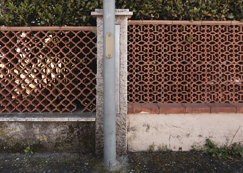 Two fences, made of terracotta bricks, in different styles, are separated by a pillar. Residential area, Italy.