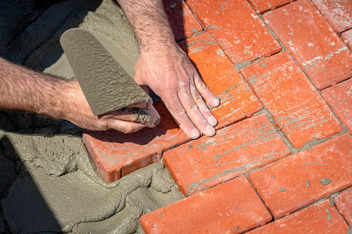 A man is laying bricks with cement on the ground.
