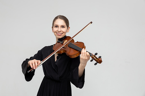 Woman musical artist playing violin isolated over light gray background, copy space