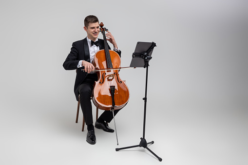 Full length of man artist wearing tuxedo playing cello with music note isolated over white background