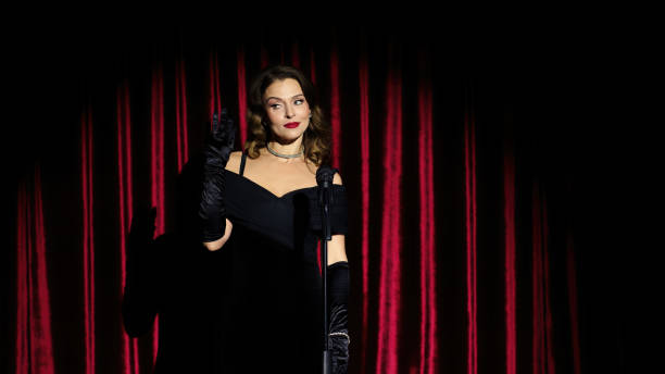 istock A young singer in a shiny black dress performs a song on stage with a microphone, in a nightclub, cabaret. A girl sings at a party on a red background. Performance at a music festival. 2150705574