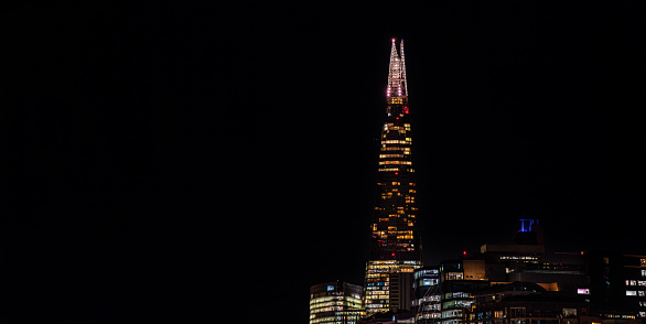 The Shard skyscraper illuminated at night with more buildings around it with the windows illuminated with the completely dark sky. London.