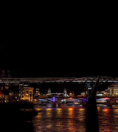 Frontal view from the River Thames of the Millennium Bridge, Blackfriars Bridge and the Tower Bridge at night, with their lights reflected in the river water. London.