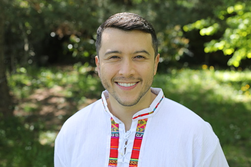A young Hispanic man in his thirties is walking around in nature. He wears a colorful traditional Latino shirt.