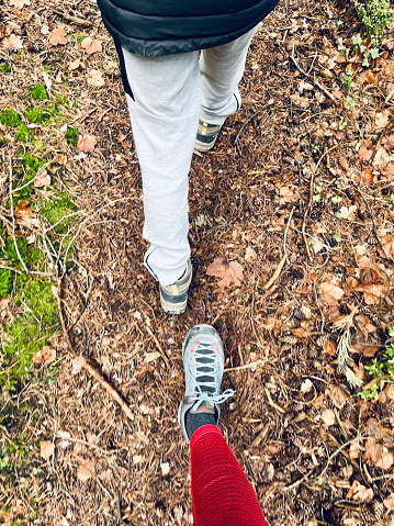 vertical photo. zenithal view. Feet walking. One foot of a child and one of an adult (woman). ground covered with leaves and earth. narrow mountain path. Sport shoes. hiking in the mountains. walk in line. autumn, winter.