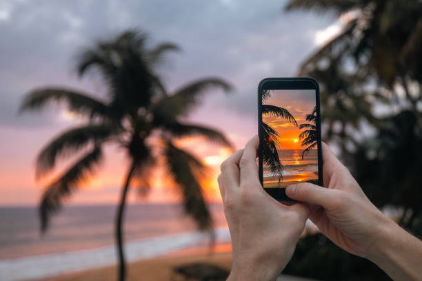 Man photographing sunset over ocean with mobile phone