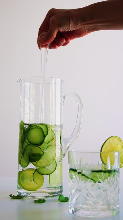Woman's hand mixing detox water with cucumber and lime in a cocktail steer