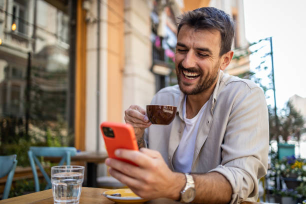 istock Stylish young man in casual clothes is using smartphone and enjoying coffee 2150721885
