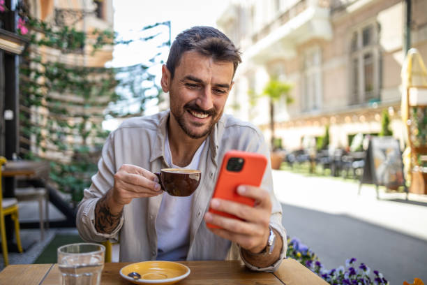 istock Stylish young man in casual clothes is using smartphone and enjoying coffee 2150721897