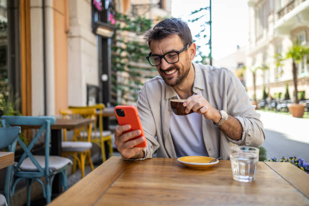 istock Stylish young man in casual clothes is using smartphone and enjoying coffee 2150721915