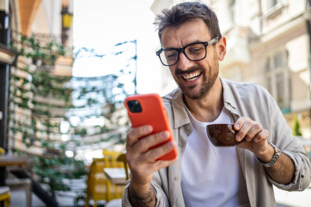 istock Stylish young man in casual clothes is using smartphone and enjoying coffee 2150721934