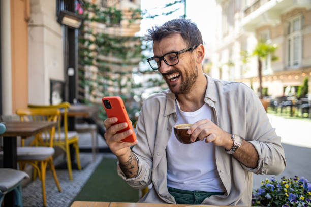 istock Stylish young man in casual clothes is using smartphone and enjoying coffee 2150721967