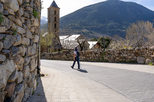 Woman walking with a backpack at the entrance of a beautiful mountain village on a trekking day on a spring morning