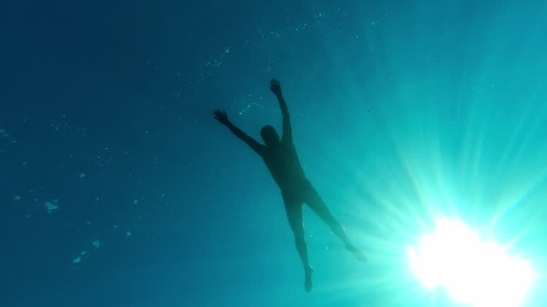 Underwater shot. A man is floating on the surface of the water against the background of the sky and the sun, looking at the seabed and fish.