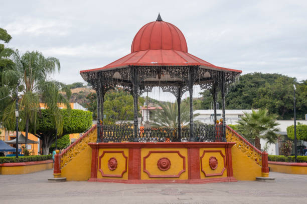 A red and yellow pavilion with a red dome sits in a park. The pavilion is surrounded by trees and has a fountain in the middle. The scene is peaceful and inviting, with a sense of tranquility
