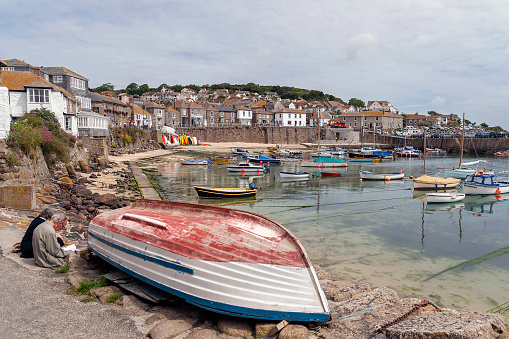 View across the harbour at Mousehole Cornwall, UK.  Boats can be seen moored in the harbour and people can be seen on the promenade