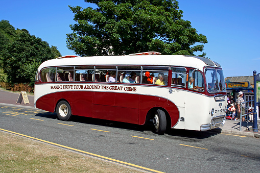 View of an old tour bus in the centre of Llandudno, UK.  People can be seen on the bus and on the promenade.