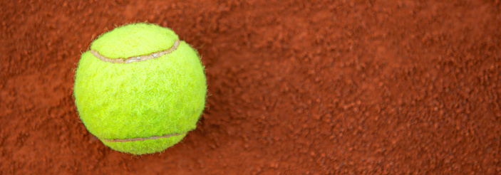 Vibrant yellow green tennis ball resting on a rustic clay court. This sports image captures the essence of tennis match on clay surface. Copy space. (10k wide image)