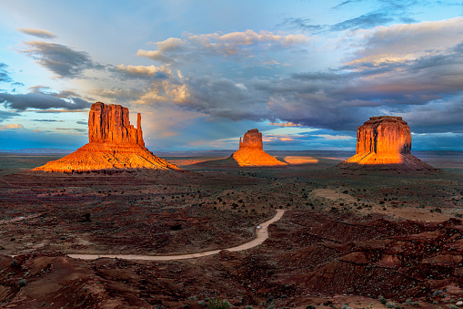 Dramatic view of the Monument Valley's magnificent butte and mittens lit up during a sunset and framed by colorful clouds from a passing storm.