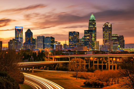 Charlotte skyline at sunset / dusk with a beautiful cloudscape in the background and a highway interchange with light trails in the foreground.
