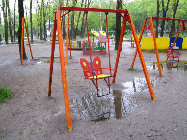 Empty swing in public park outdoor kid playground, wet rainy day, rain and puddles.