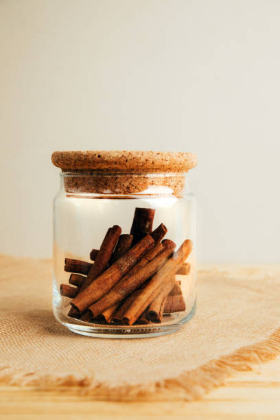A cinnamon stick in glass jar on a light wooden background.  Spices, herbs. Front view, selective focus