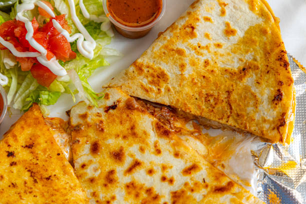 An unrecognizable woman enjoys eating a quesadilla on a restaurant patio.