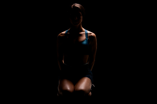 Female runner backlit abstract silhouette. Girl in sportswear posing against dark background.