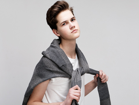 young handsome teenage hipster guy wearing sweater posing against white background isolated