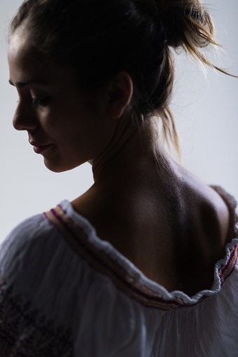 Artistic studio portrait showcasing a young woman in a delicate pose, subtly lit from behind to emphasize her features and expressions.