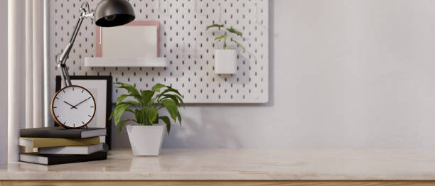 istock A tabletop with books, a clock, a table lamp, a potted plant, and a space against the wall. 2150765234