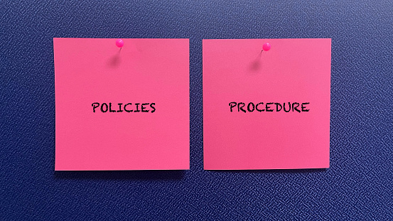 Words Policies And Procedure on pink sticky note with blue background.