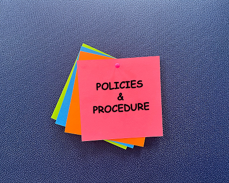 Note with Policies And Procedure. Sticky note pined on a bulletin board.