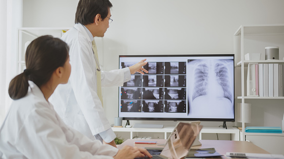 Asian medical team, consisting of a male and female doctor, analyzing diagnostic imaging results on a digital screen in a clinic.
