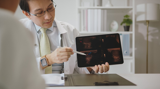 A doctor in a white coat uses a stylus to go over medical imaging on a tablet, ensuring the patient understands the details of the diagnosis.
