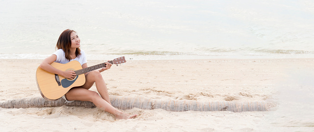 Banner Young women playing acoustic guitar on the beach. Happy Woman person playing acoustic guitar music instrument seaside sit on sand tropical beach island. Happy guitarist hobby with copy space