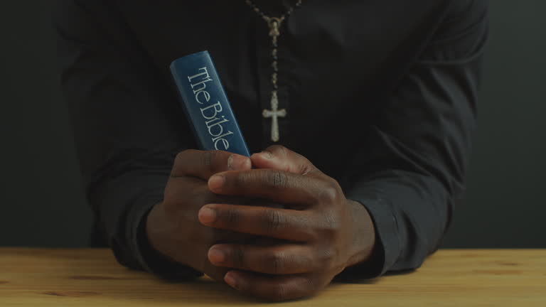 Hands of Catholic Priest Holding Bible at Wooden Table during Prayer